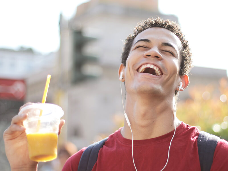 A laughing boy with headphones and juice in his hands