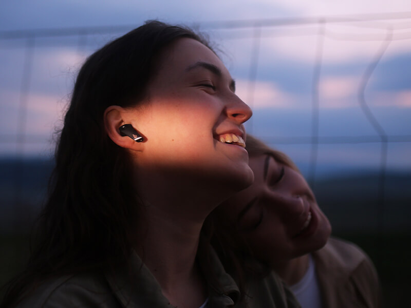 Two smiling girls leaning together and wearing edifier headphones