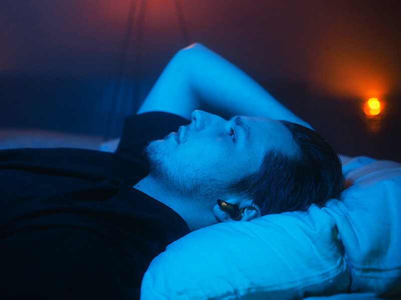 A man lying on the bed, wearing edifier earbuds